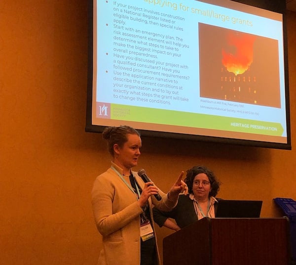 Gillian Maguire and Megan Narvey at the podium presenting with a screen showing a PowerPoint presentation behind them