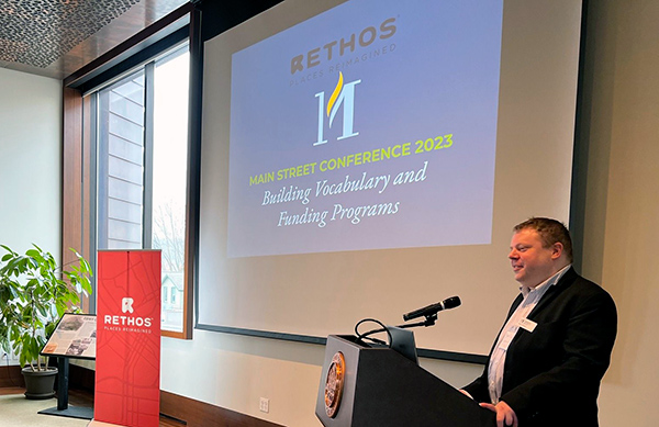 Ryan Maciej presenting at the Main Street Conference , PowerPoint display is to the side of him showing title card of presentation