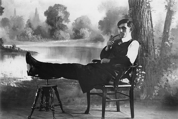 Man sitting in chair with feet up on stool smoking pipe