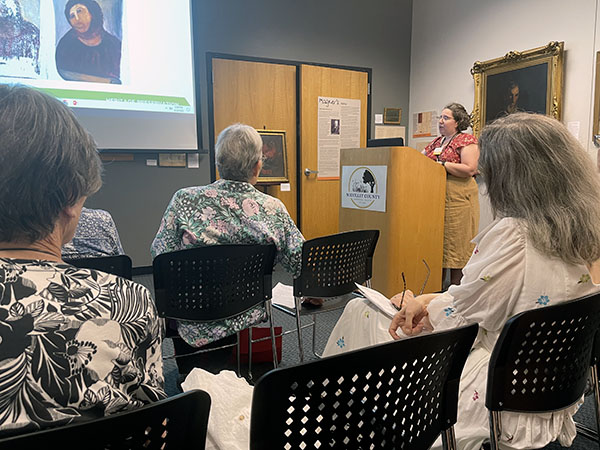 Presenter at podium with two rows of audience members in foreground