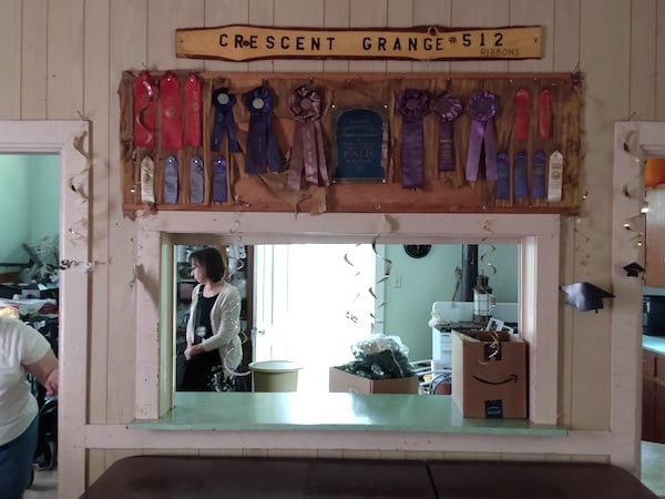 Photo looking kitchen serving windown opening from grange hall, Ribbon awards are above window and a sign saying CRESENT GRANGE 512 above the ribbons.