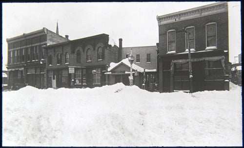 Four buildings line a wintery street scene, with snow piled up in the foreground.