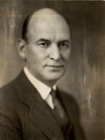 The head and shoulders of bald man wearing a collar, tie, and suit jacket.