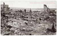 Rocks, charred tree stumps, and building ruins stretch to a distance horizon with a lake to the right. The walls of two burned buildings still stand.