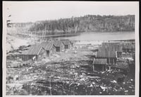 Log structures on a deforested piece of land next to a river.