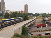 A light-rail train crosses a bridge over a freeway as vehicles pass underneath.
