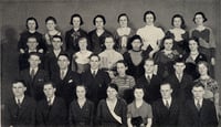 Students stand in four staggered rows of six or seven people each. They wear formal dresses and suits.