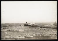 Waves crash toward a beach on two sides of a pier, with a block of white sky above.