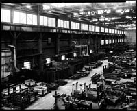 Multiple-story factory interior with dozens of vehicles on the floor.