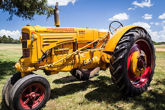 Three-wheeled tractor with a yellow body sitting on green grass in front of a blue sky in the background.