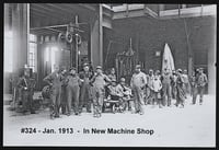 Adults and children stand in an open space in front of a factory building.