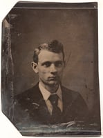 Tintype photograph of 3/4 view of a man. He is wearing a jacket, tie, and a shirt with a white collar
