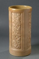 Tan ceramic cylinder with panels of relief carvings of vines.