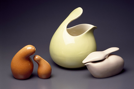 Orange salt-and-pepper shakers, a yellow pitcher, and a taupe oil pourer in fluid, round shapes sit against an indigo background.