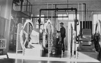 Black and white photograph of Assistant keeper Tom Hassing standing next to diesel air compressors at Split Rock Lighthouse c.1945.