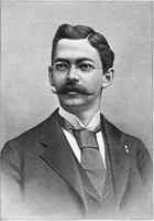 Head, shoulders and chest of a mustachioed man wearing glasses and a wide tie. 