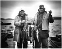Two men stand side-by-side on a boat dock to hold up fish strung onto a line.