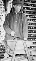 Black and white photograph of Martin Carlsted turning the handle of a manual corn grader to grade and separate different sizes and shapes of kernels, c.1910.