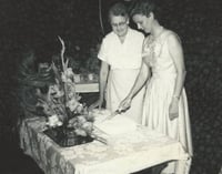 Black and white photograph of BPWC president Mary Louise Jorgenson (right) cuts cake for Ida Twedten (center), the first BPWC president, at a birthday party held for Twedten, 1966.