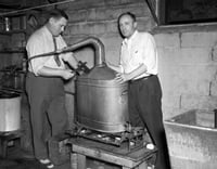 Black and white photograph of two men breaking apart an illegal still,1940. Photographed by the Minneapolis Star Tribune.