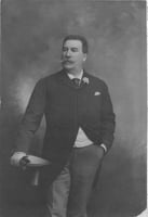 Photograph of Emile Amblard leaning on a table, holding his gloves and wearing a boutonniere. Circa 1910.