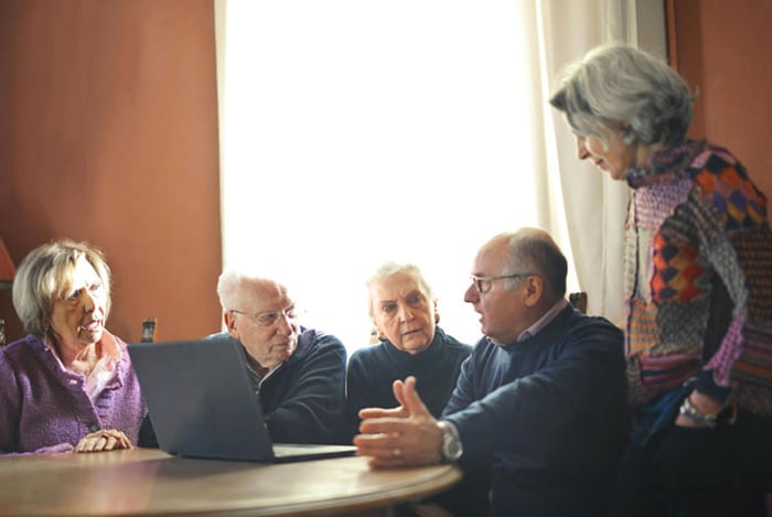 Elderly people sitting at table with laptop.