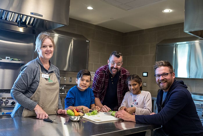Three adults and two kids around a kitchen prep table.