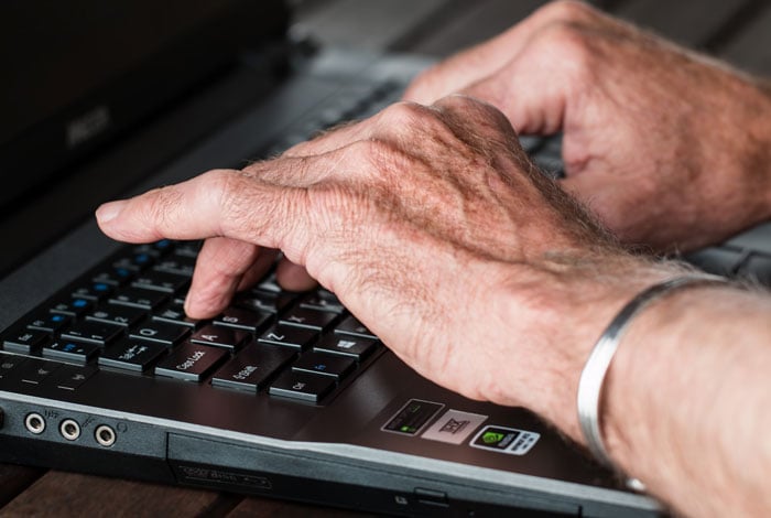 Old hands typing on laptop.