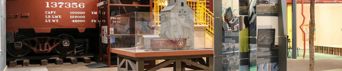 A small-scale display of a grain mill sits in front of a boxcar.