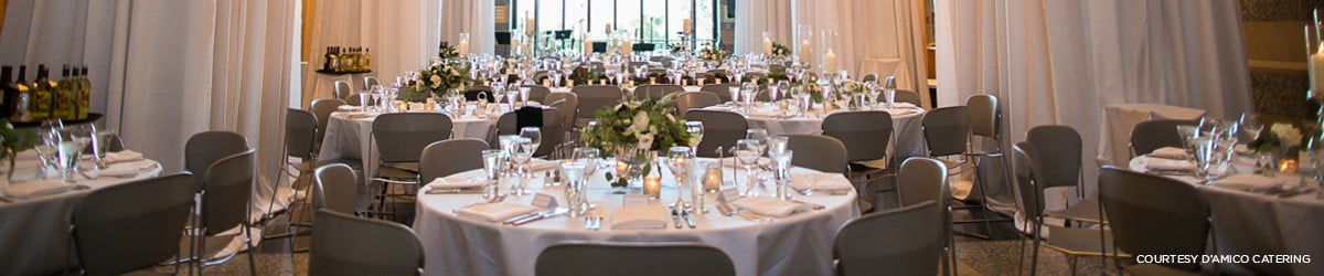 Several round tables are set with fine linens, crystal stemware, and floral centerpieces in preparation for a formal event.