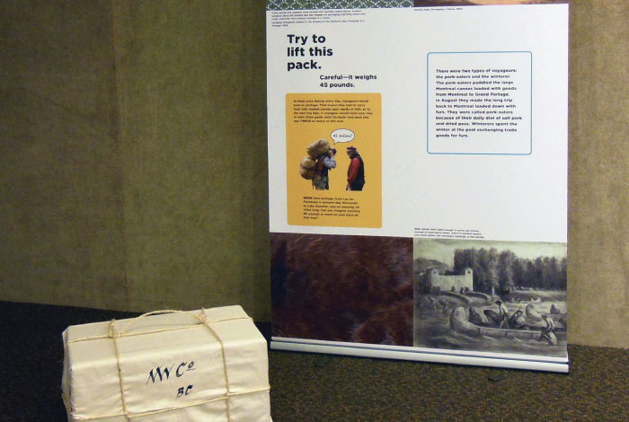 A package sits in front of an exhibit sign saying "Try to lift this pack."