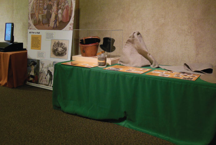 A table with several hats displayed on it sit next to a display board.