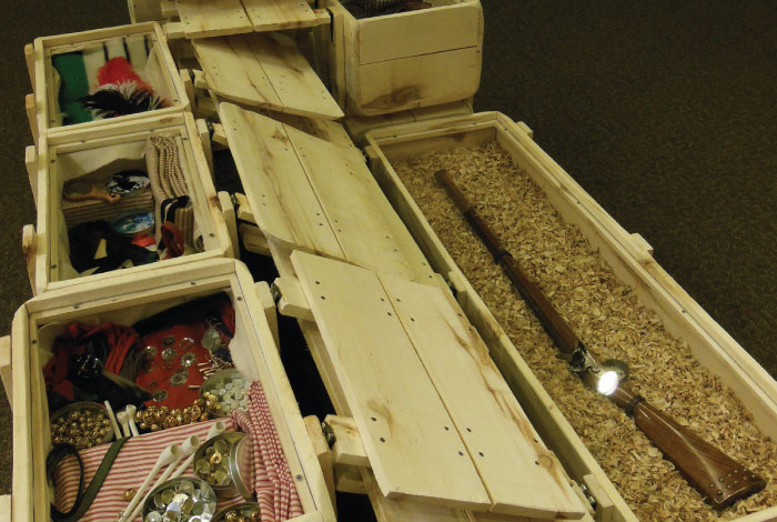 Trade good crates filled with a rifle, blankets, and other goods.