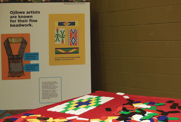 A close-up view of a table with colorful tiles in front of a sign for beadwork designs.