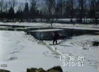 Water covered with ice and snow on top of it, with oil-filled water in the middle ground, and trees in the background. 