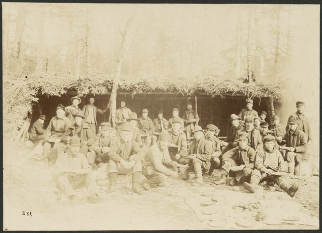 Sepia-toned photograph of lumber camp worker eating a meal outdoors.