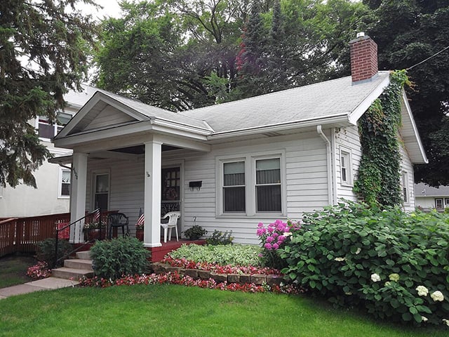 A one-and-a-half-story bungalgow with two two columns supporting a front porch. The house and its columns are painted white.