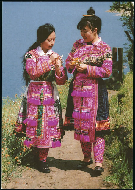 Color scan of a Hmong New Year postcard showing two young women in traditional Hmong dress, c.1980s.
