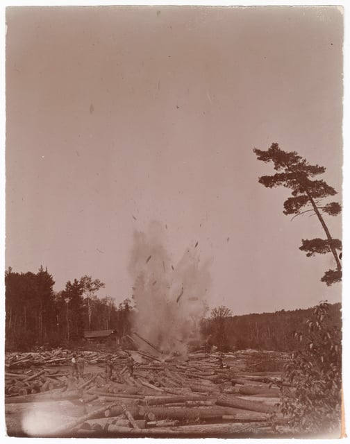 An explosion in a log-choked river throws up water and wood into the air.