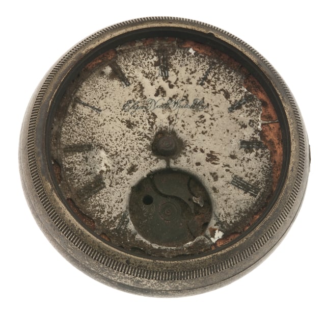 The face of round pocketwatch destroyed by fire sits against a white background.
