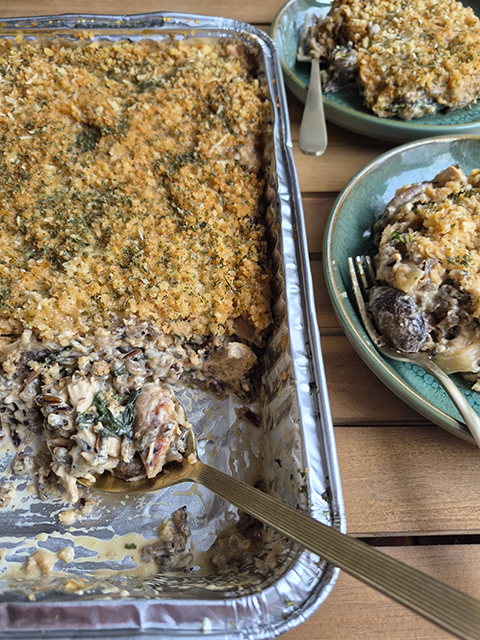 A metal tray of hotdish with a spoonful at left, and two plates of the food at right.