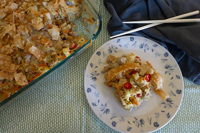 A serving of hot dish sits on a white, flower-sprigged plate next to a baking dish with more hotdish inside.