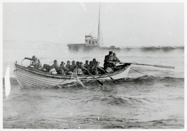 A rowboat full of people navigates with outstretches oars towards a ship in the background.