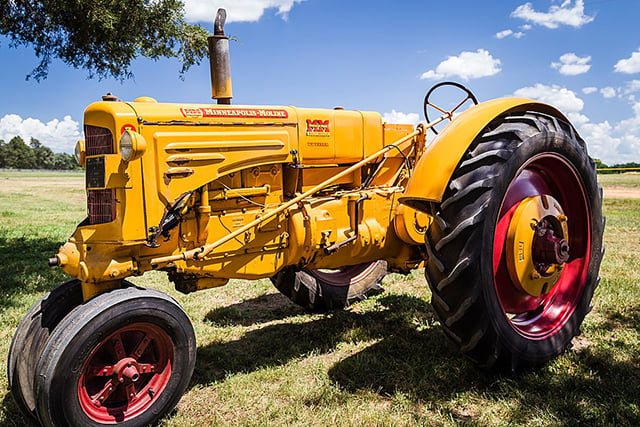 Three-wheeled tractor with a yellow body sitting on green grass in front of a blue sky in the background.