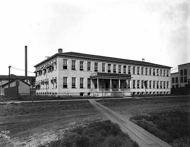 Rectangular two-story building with a columned front porch under white sky.