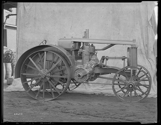 A four-wheeled 1920s tractor in front of a cloth backdrop.