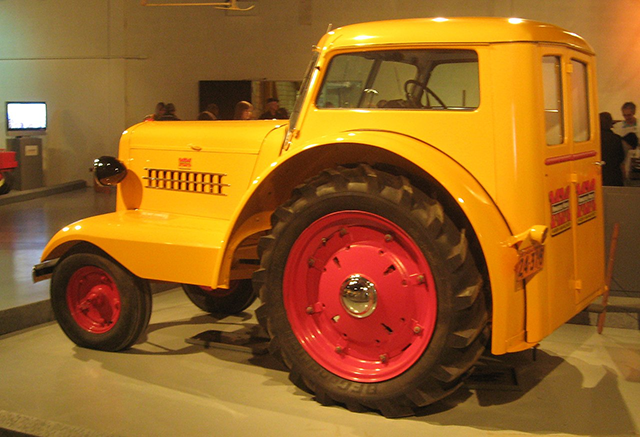 A yellow tractors with four tires with red rims inside a warehouse space.