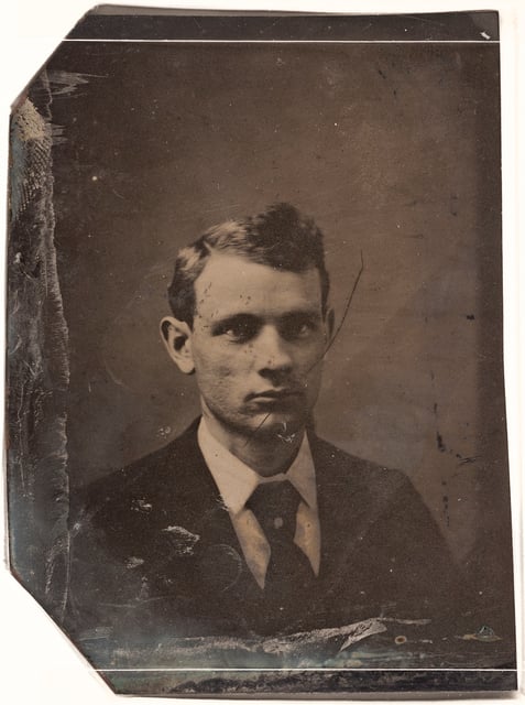 Tintype photograph of 3/4 view of a man. He is wearing a jacket, tie, and a shirt with a white collar