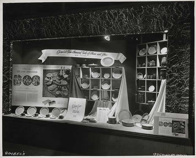 Ceramic plates in recessed boxes and on a lower shelf sit behind a pane of glass.