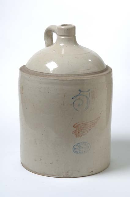 A cylindrical jug with a round top leading to a grooved spout and a handle.